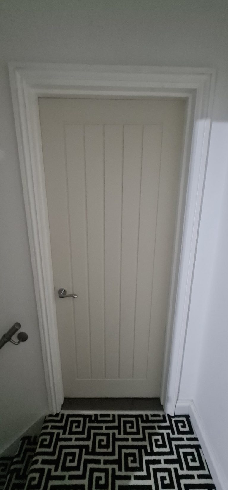 A plain, light-coloured wooden door with vertical panels, set in a corridor.