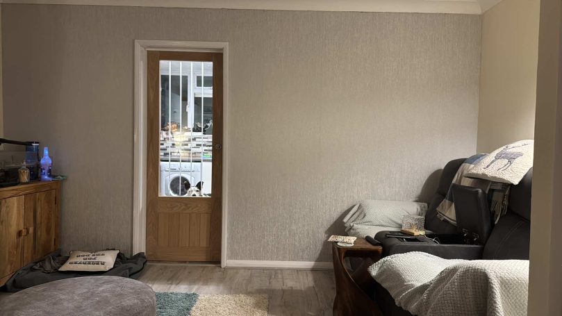 Living room with Oak vanere and large glass pane door. Wallpapered feature wall. Wooden floor.