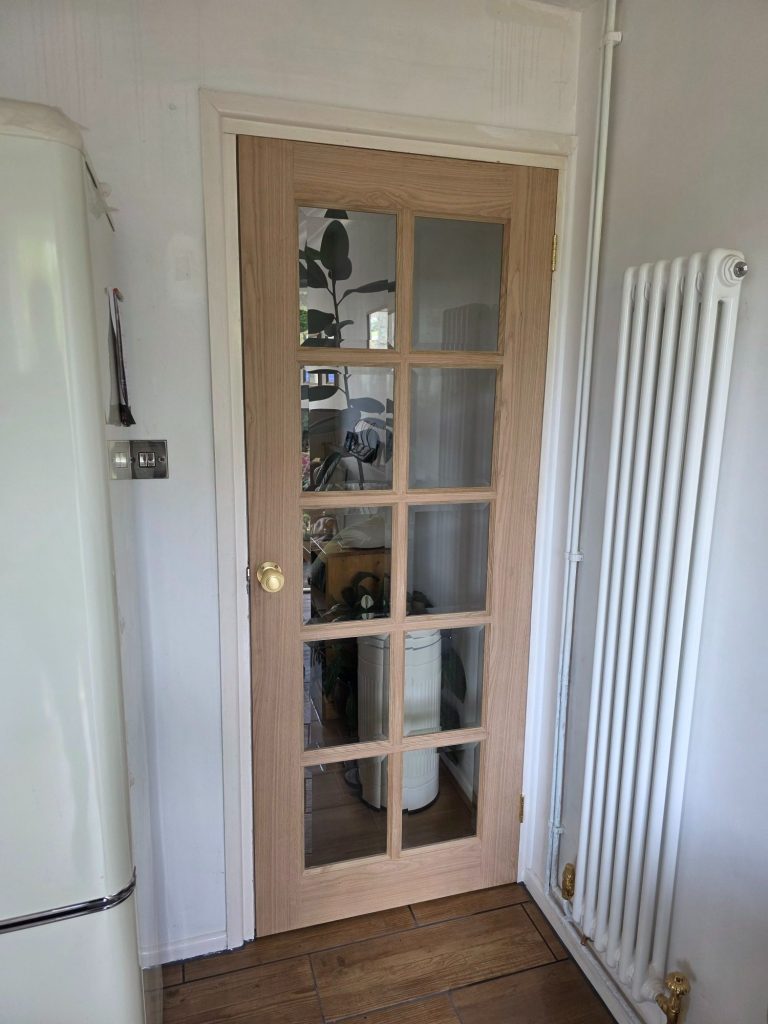 Interior oak veneer 10 panel glass door with brass hardware separating a kitchen and living room.