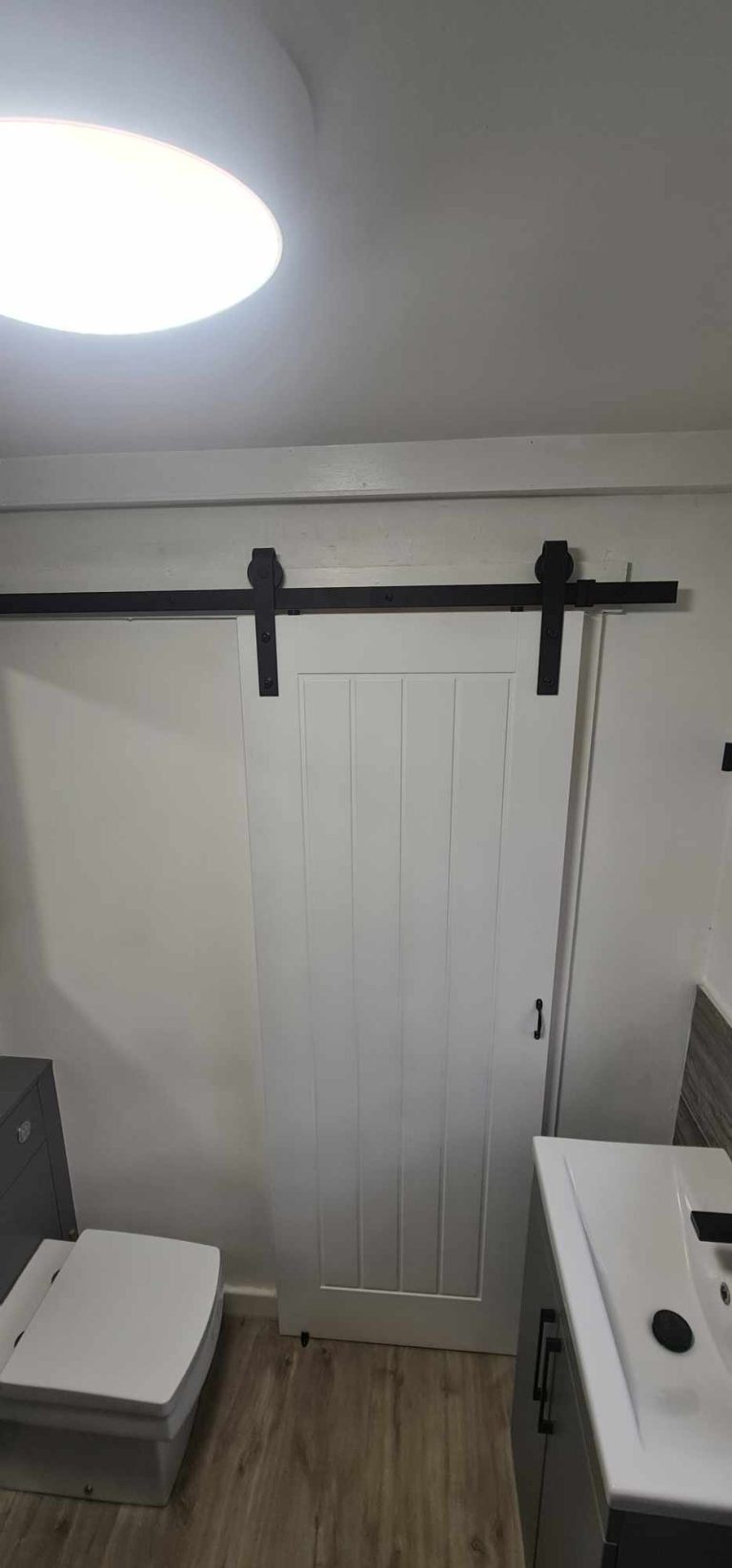 Modern bathroom with sliding barn door, sink, and toilet in a minimalist setting.