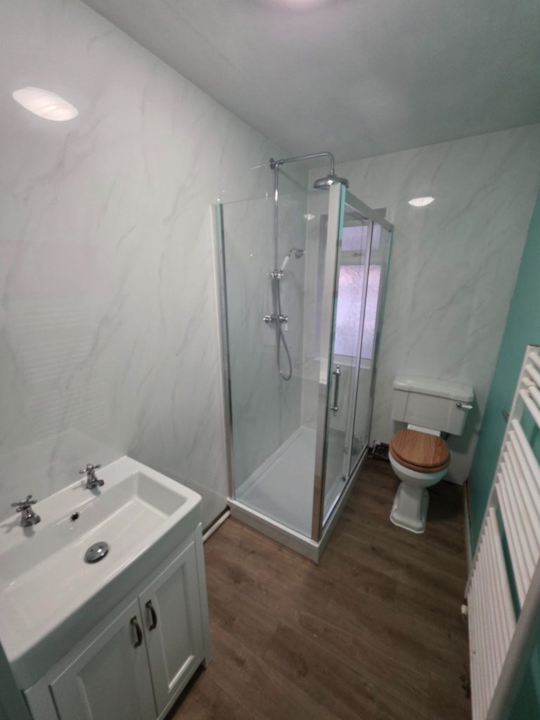 Modern bathroom featuring a shower cubicle, toilet, sink, and marble effect wall panels.