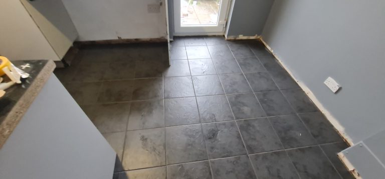 Square black tiled floor in a room with grey walls and a door to the outside.